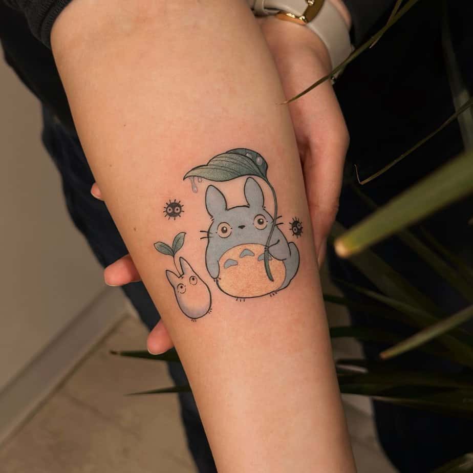 Totoro holding a leaf umbrella with small Totoros beside him